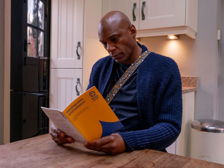 A man sits at a kitchen table as he reads a Marie Curie booklet