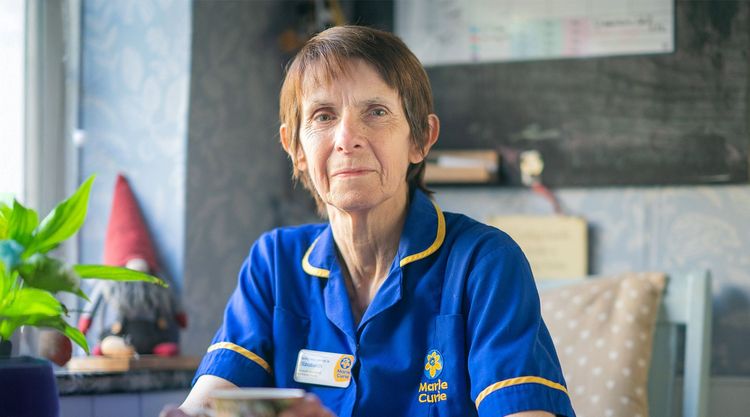 Marie Curie Nurse Liz Sherwood sits near a window, wearing a blue Marie Curie uniform.
